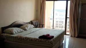 A bedroom with a bed, a chair, and a view of the outside through a window. - Parinya's Apartment (Pattaya)