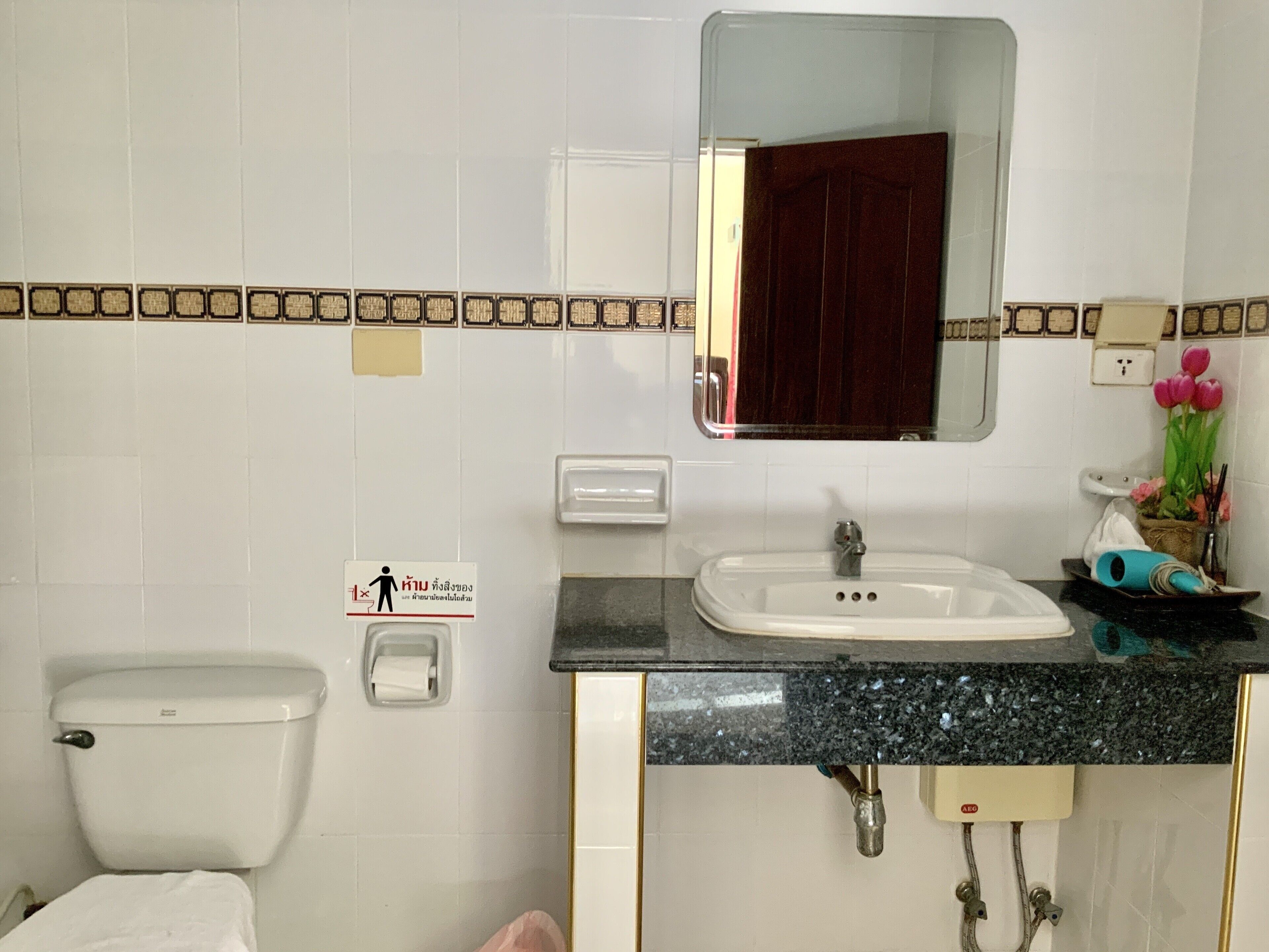 A bathroom with a toilet, sink, mirror, and a sign with a figure and text.