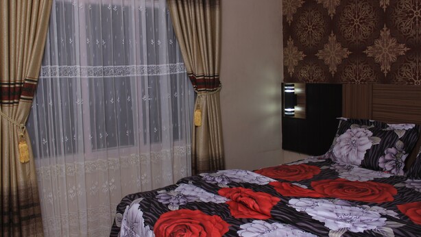 A hotel room with a bed, curtains, a wall with a floral pattern, and a television. - Novatel Yogyakarta (Yogyakarta)