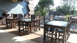 A dining area with wooden chairs and a glass table, large windows with a view of buildings and trees, and a tiled floor. - Novatel Yogyakarta (Yogyakarta)