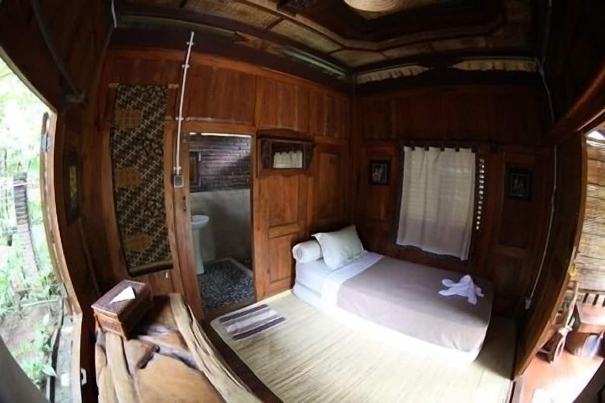 Une chambre dans un chalet en bois, avec un lit, une petite salle de bain et une fenêtre avec des rideaux.