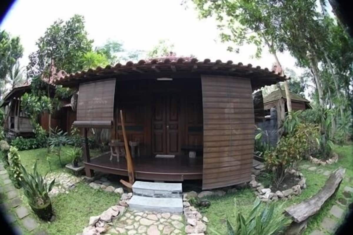 Une petite maison en bois, de style rustique, dotée d’un porche abrité et d’un chemin de pierre menant à l’entrée.