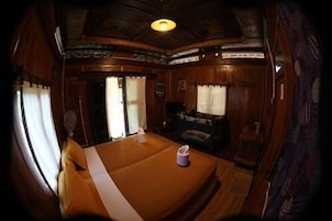 Una habitación con techo de madera, una cama, una mesita y una ventana con cortinas.