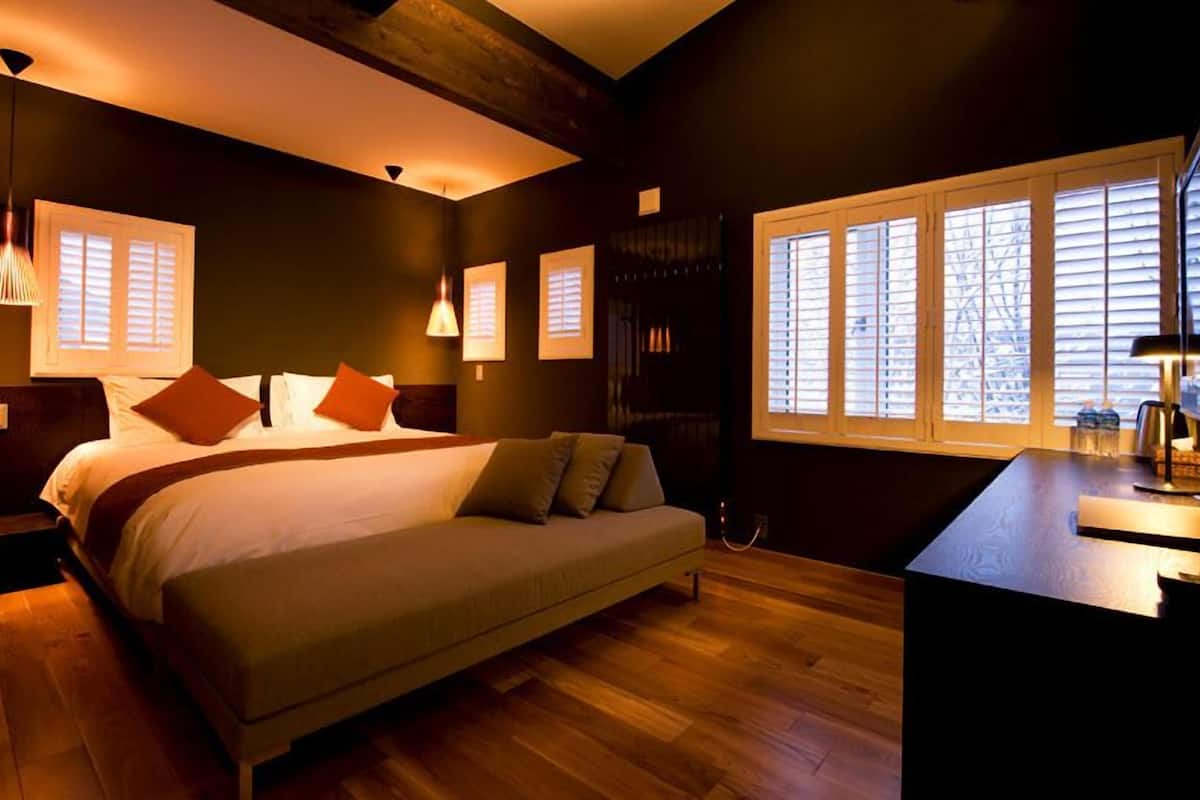 Un dormitorio moderno con una cama grande, lámparas de noche, suelo de madera y una ventana con persianas.