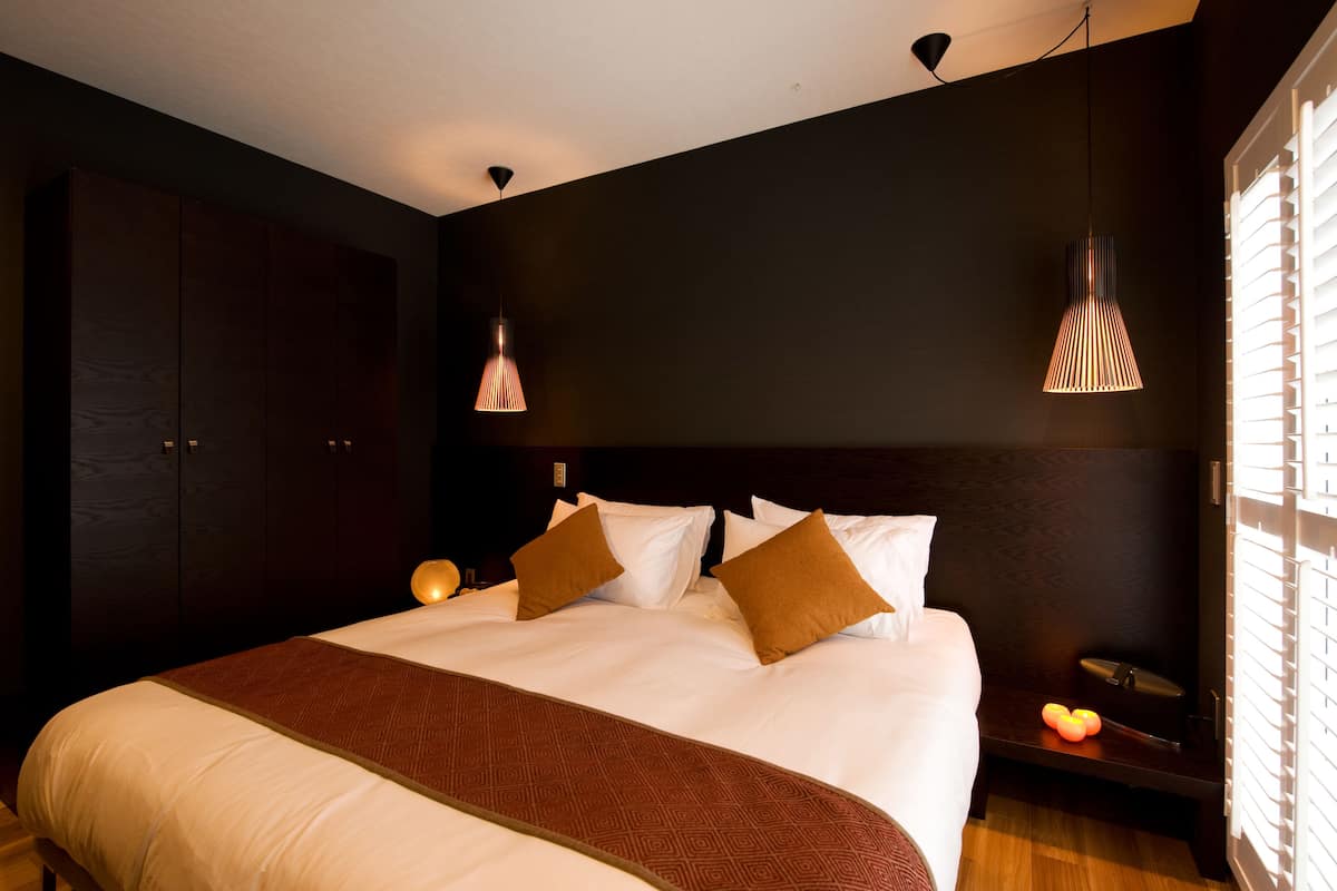 Una habitación de hotel moderna con una cama grande, paredes oscuras y dos lámparas colgantes.