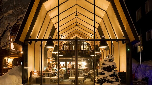 Een met sneeuw bedekte gebouw met een warm interieur, grote ramen en een sneeuwtak in de voortuin.