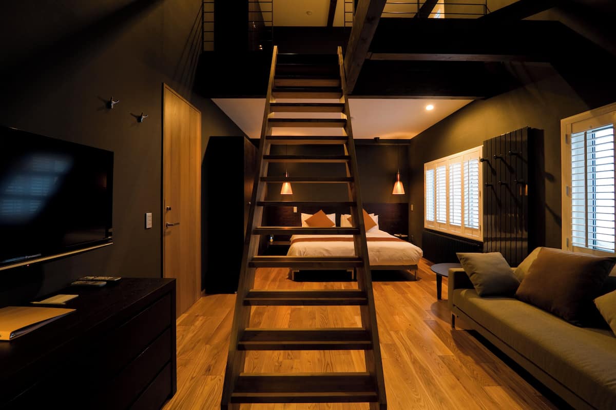 Un interior moderno con una escalera de madera que lleva a un dormitorio, un televisor y un sofá.