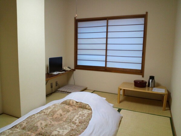 Une pièce de style japonais traditionnel, avec un sol recouvert de tatamis, un futon servant de lit, un bureau avec un ordinateur portable et une fenêtre à panneaux coulissants de type shoji.