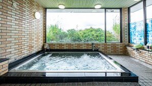 A spa area with a hot tub, brick walls, and large windows offering a view of greenery.