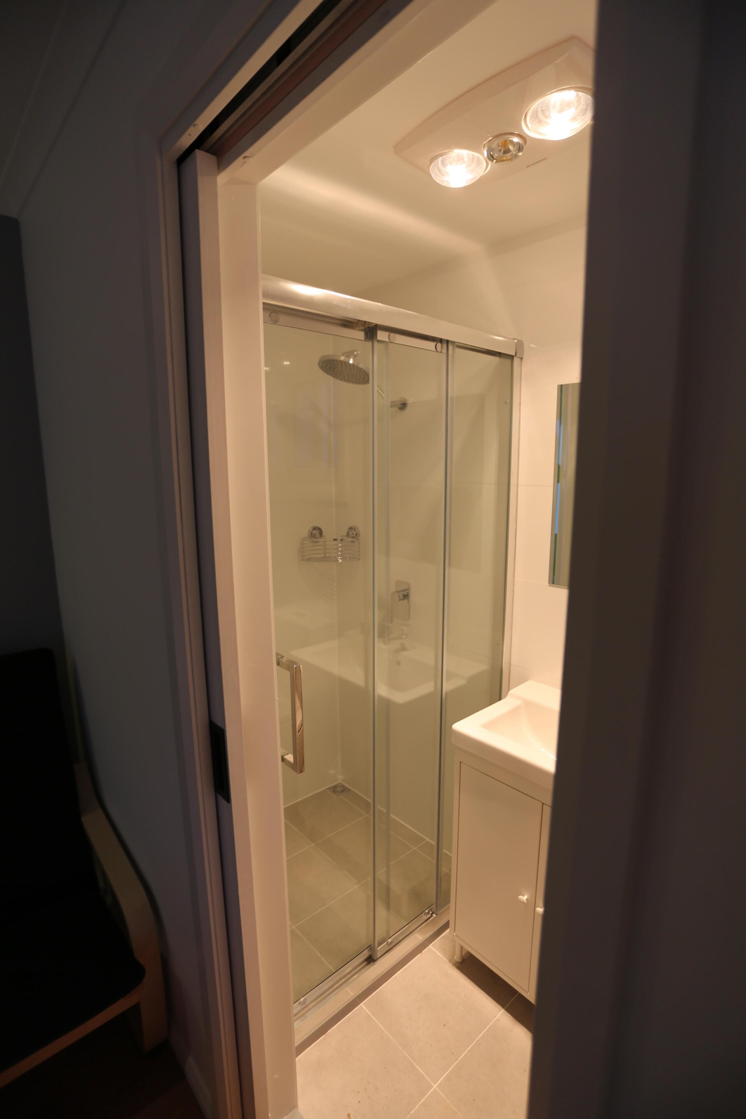 Una ducha con cerramiento de vidrio, un lavabo y un mueble blanco.