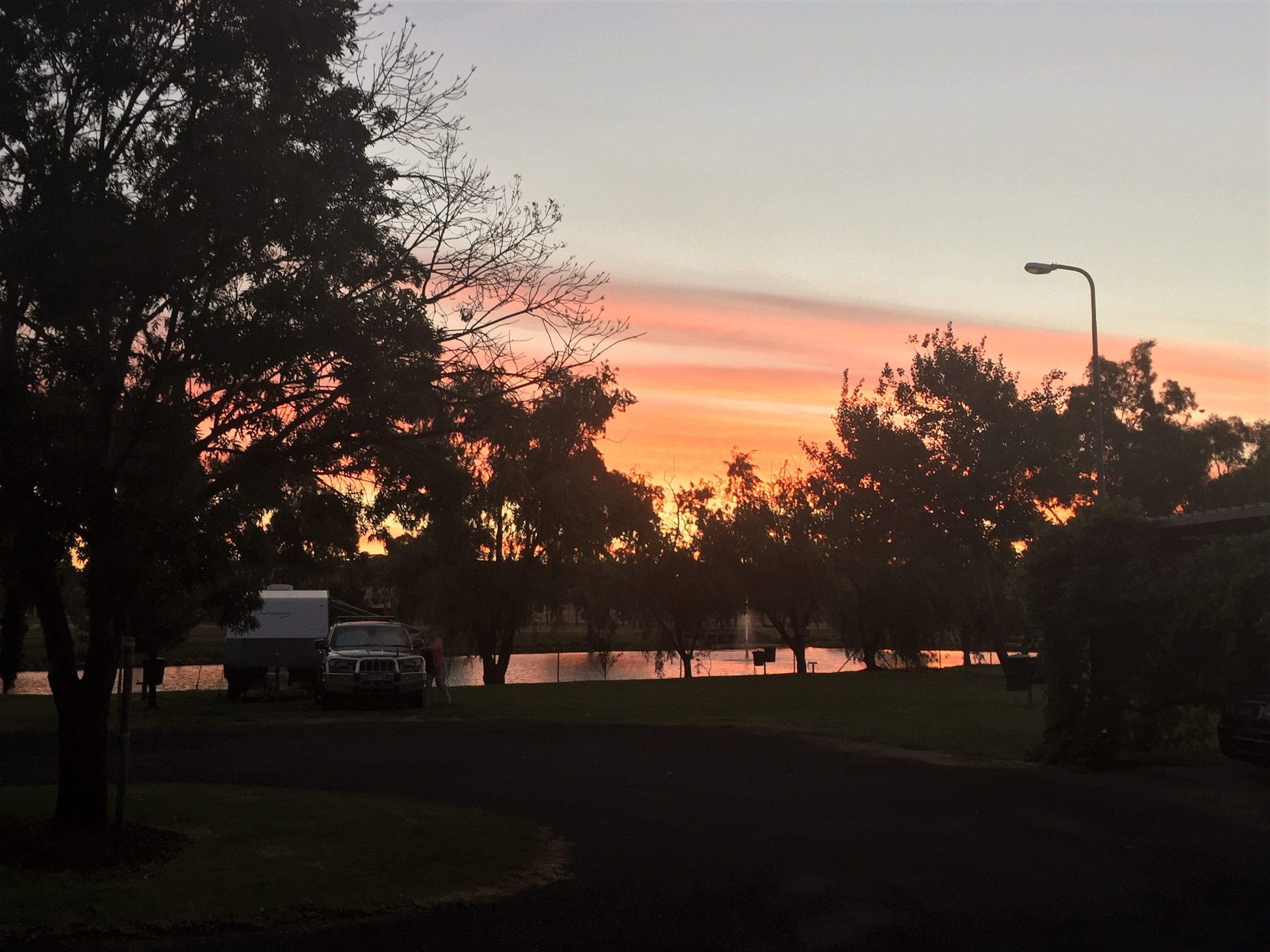 Una vista al atardecer con árboles y un vehículo estacionado.