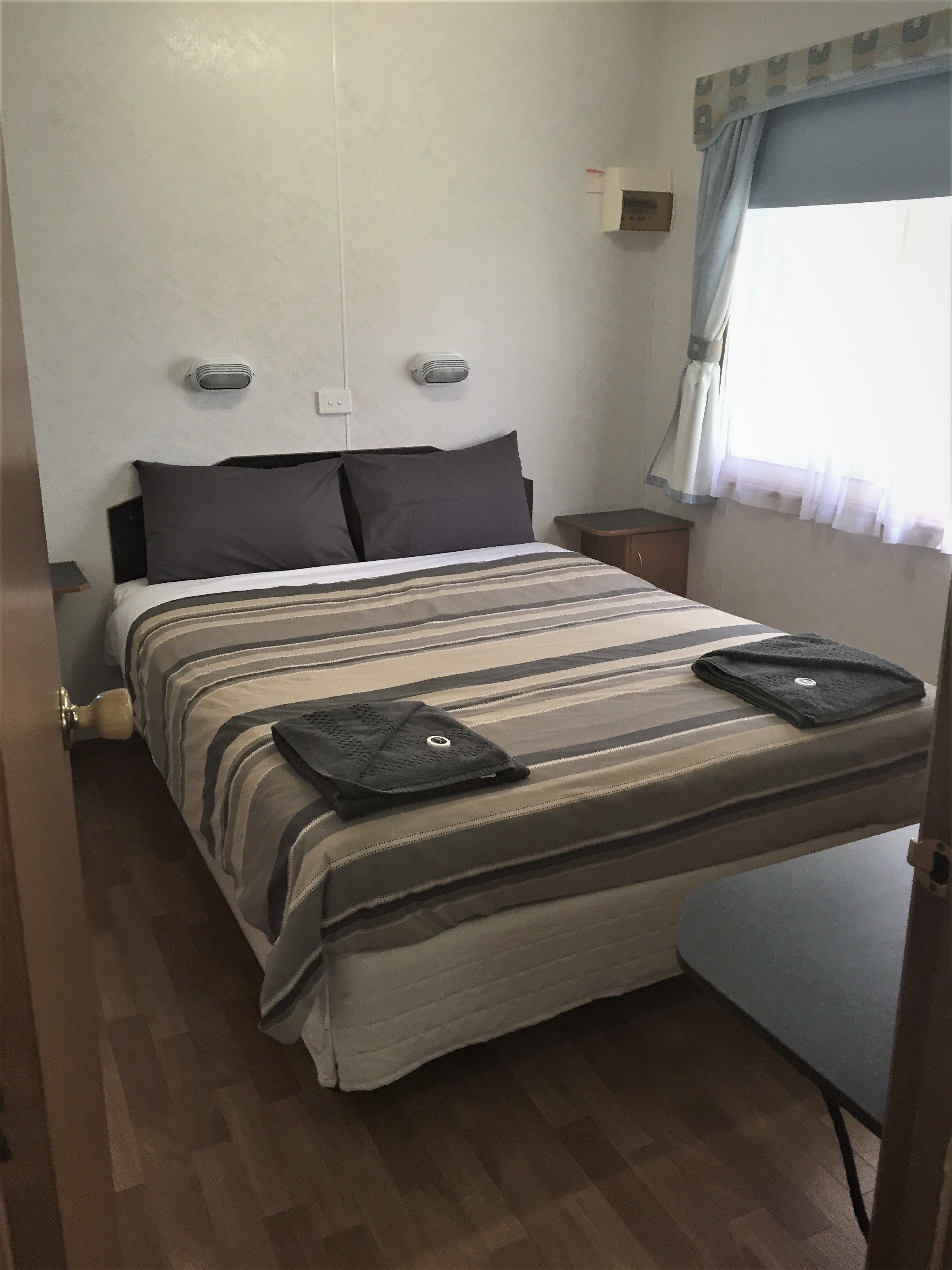 A bedroom with a bed, bedside tables, a window with curtains, and a wall-mounted heater.