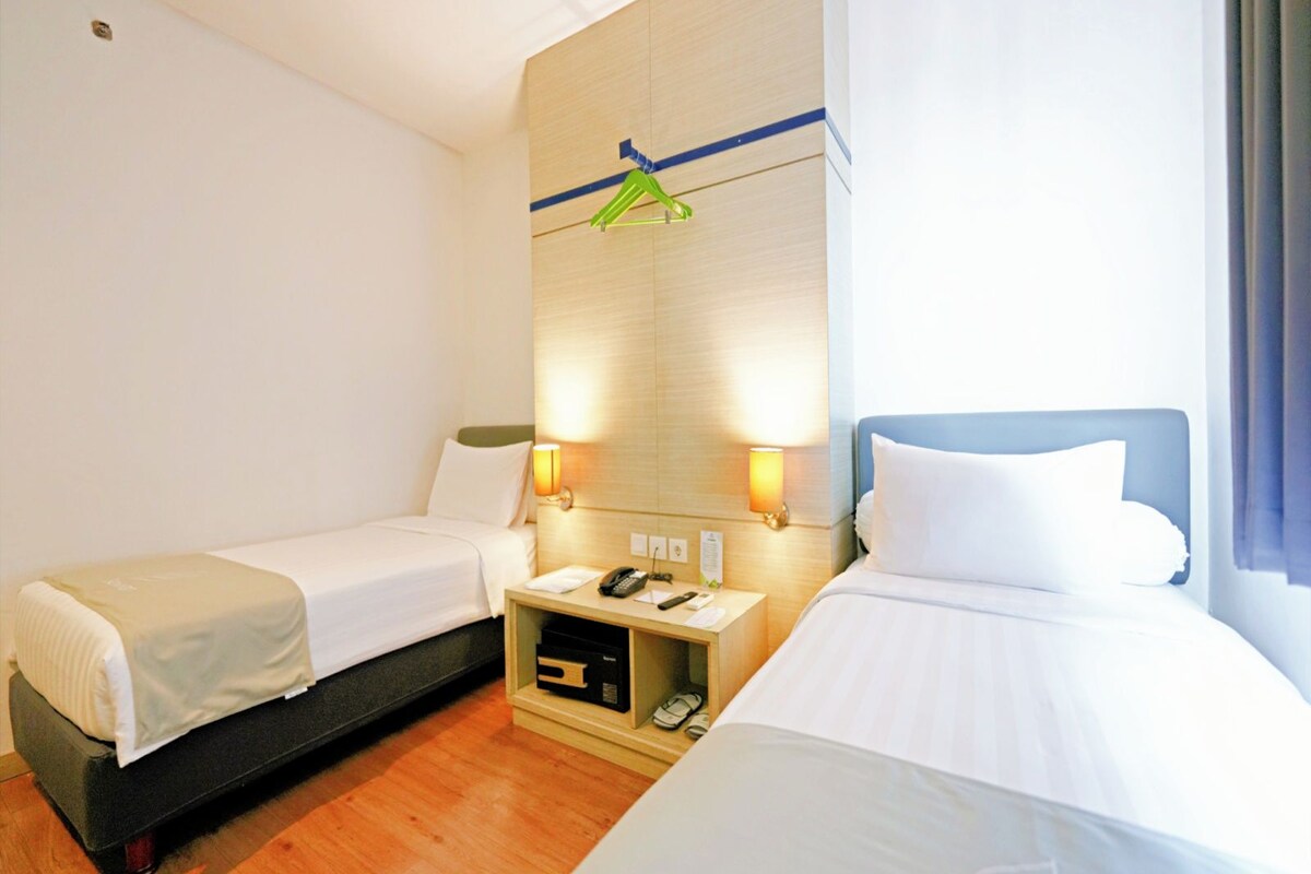 Une chambre d’hôtel avec deux lits simples, une table de chevet avec une lampe et un porte-manteau fixé au mur.