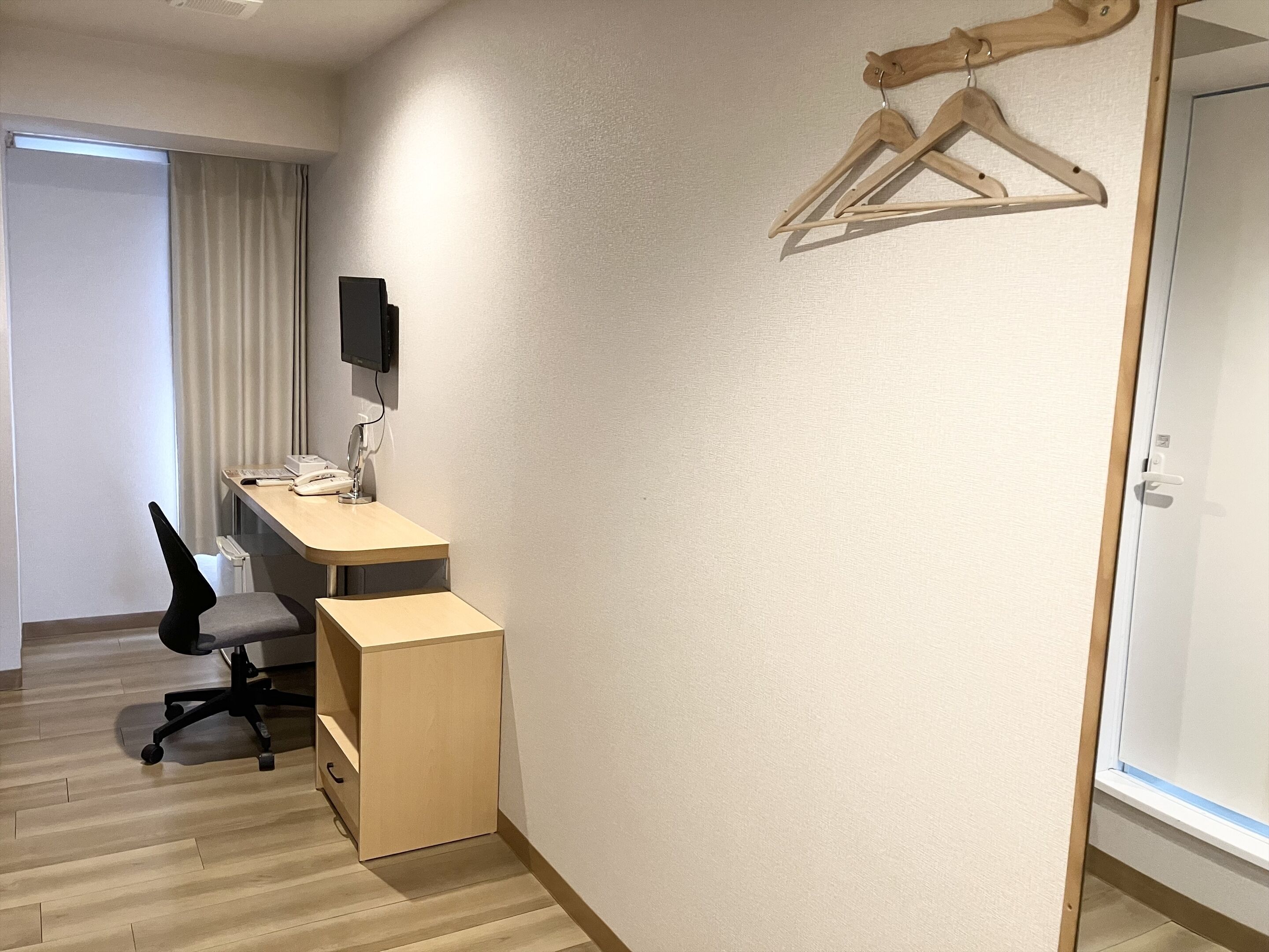 A small, well-lit room with a desk, chair, and wooden hangers on the wall.