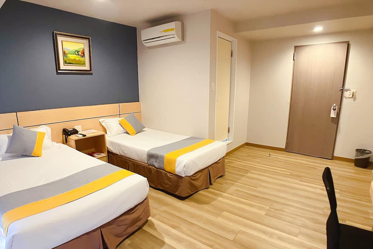 A hotel room with two beds, a desk, a chair, a door, and an air conditioning unit.
