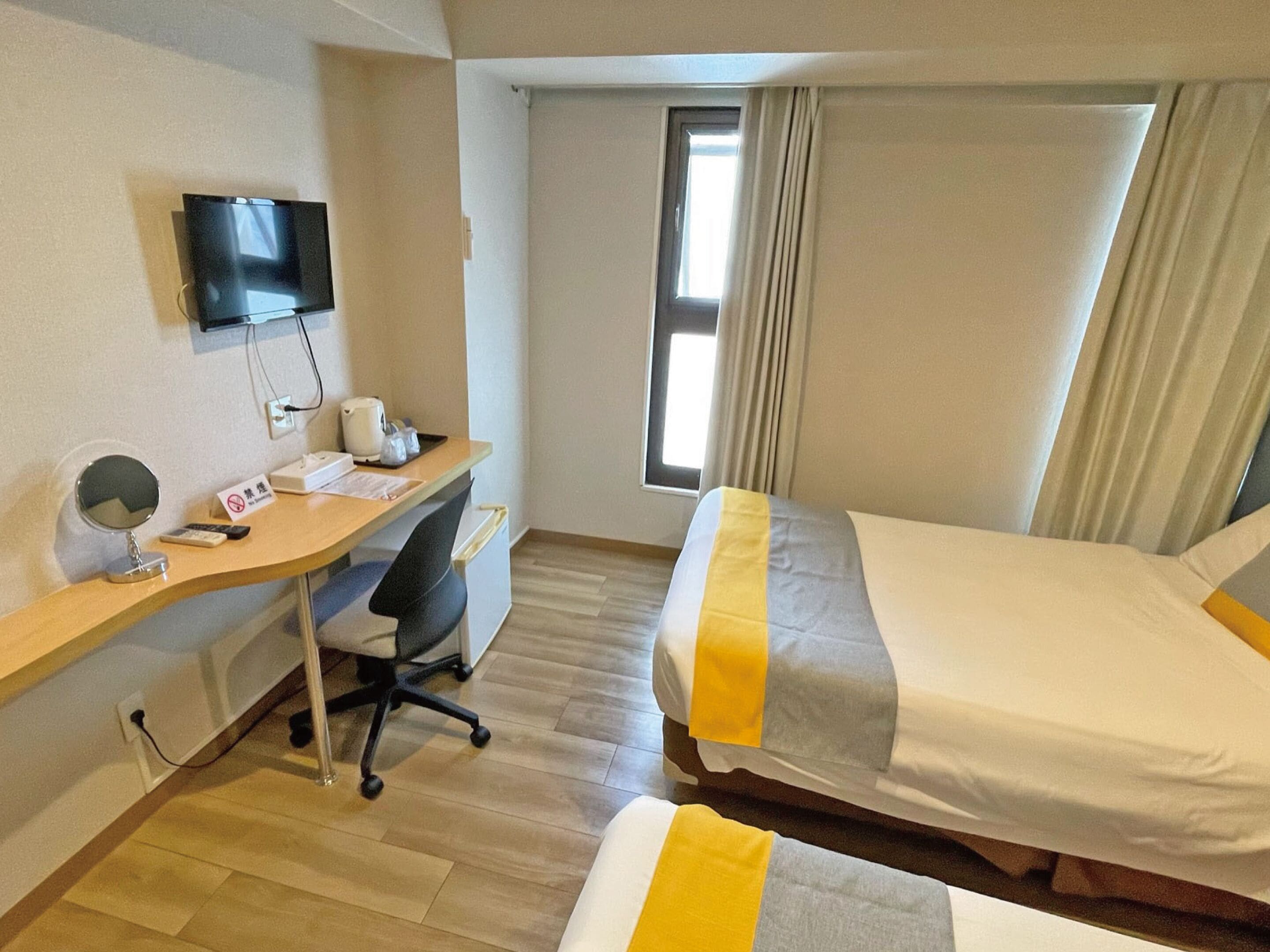 Een hotelkamer met een bureau, stoel, twee bedden, een televisie en een raam met gordijnen.
