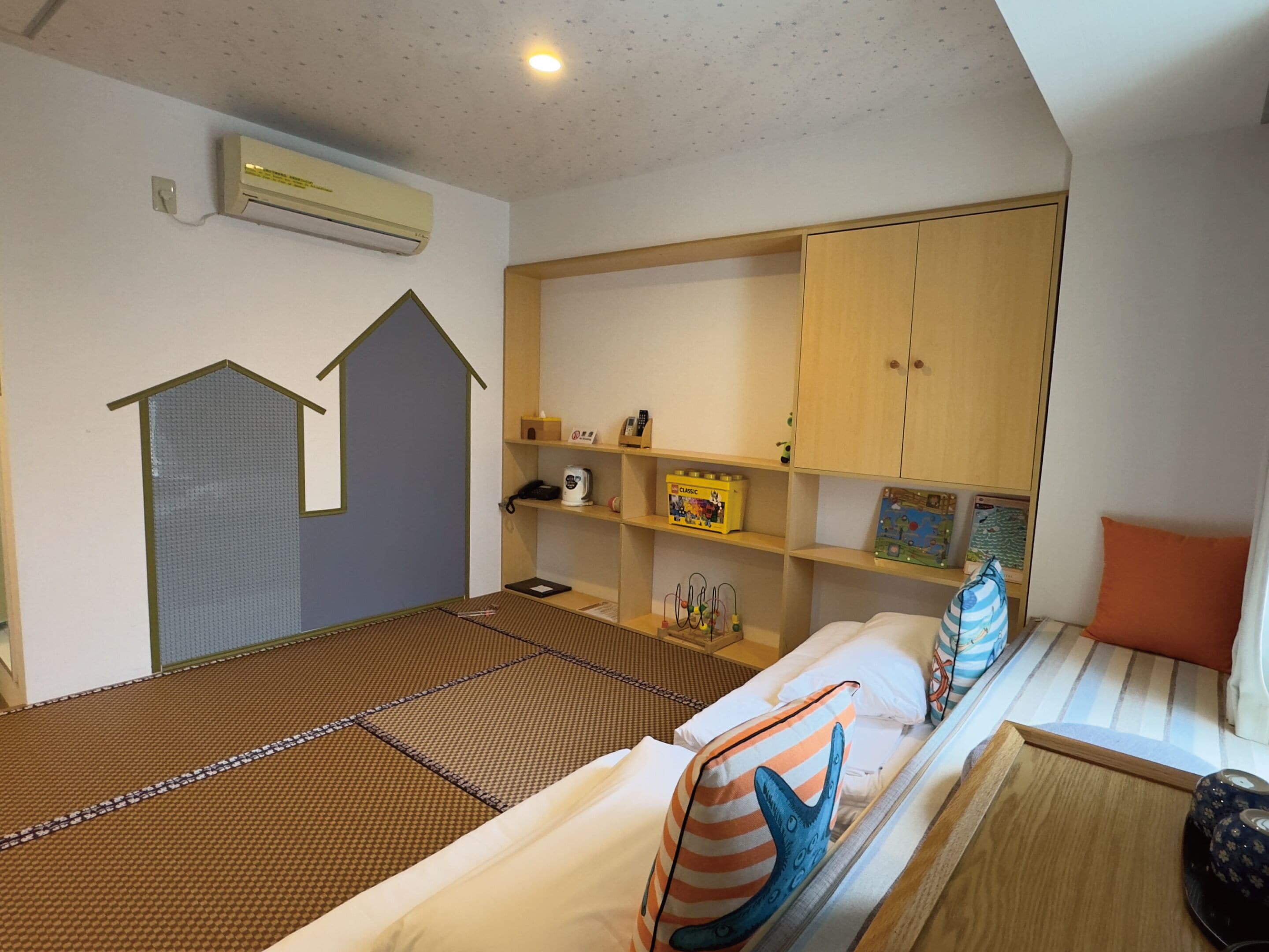 Une pièce avec un futon servant de lit, une petite maison de jeu, une étagère remplie de jouets et un placard.