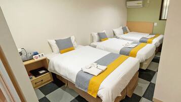 Habitación de hotel con tres camas individuales, un escritorio pequeño con una silla y aire acondicionado instalado en la pared.