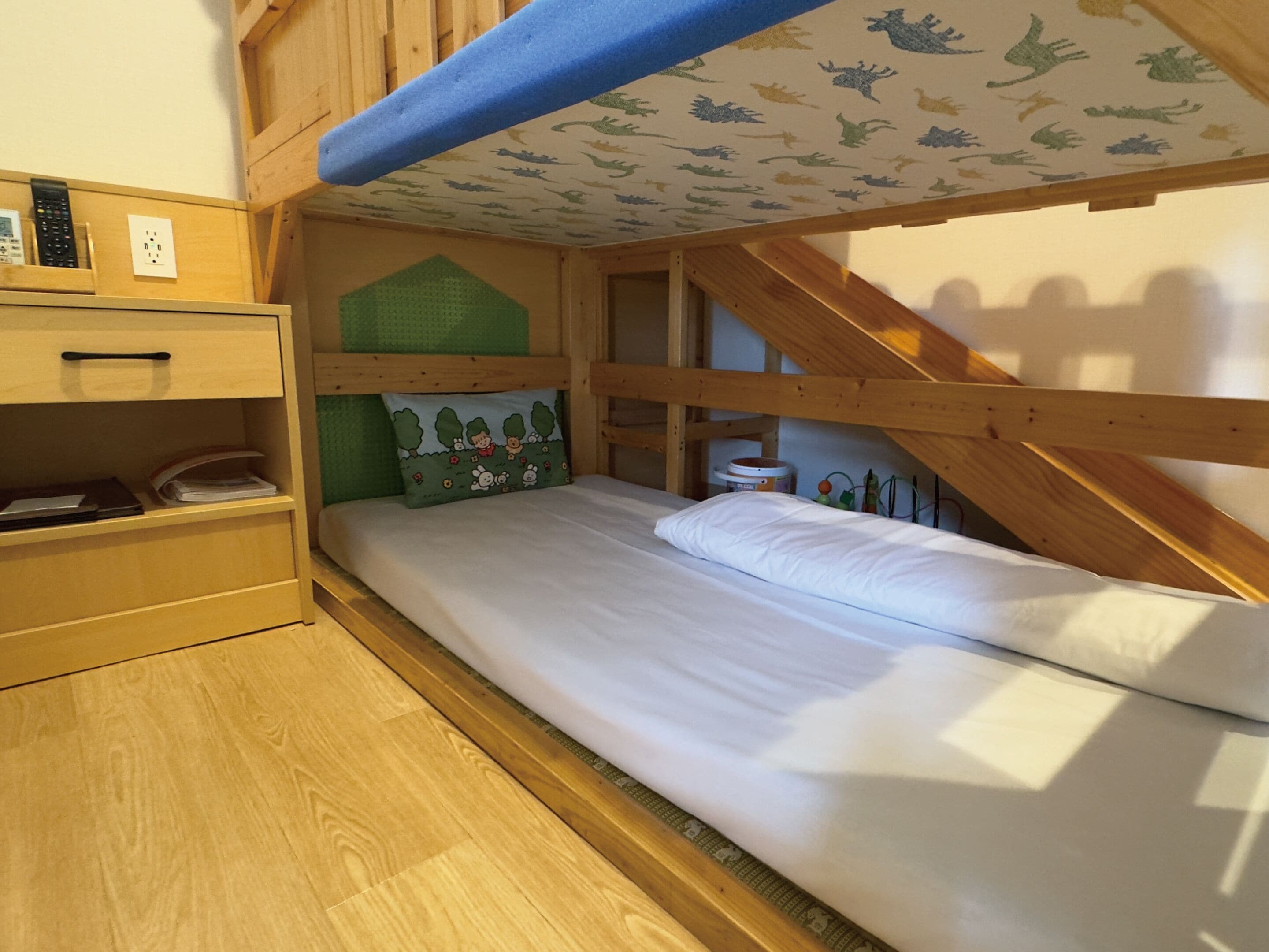 Un letto a castello con testiera verde, una scrivania in legno con un telefono e un piccolo ripiano con libri e documenti.