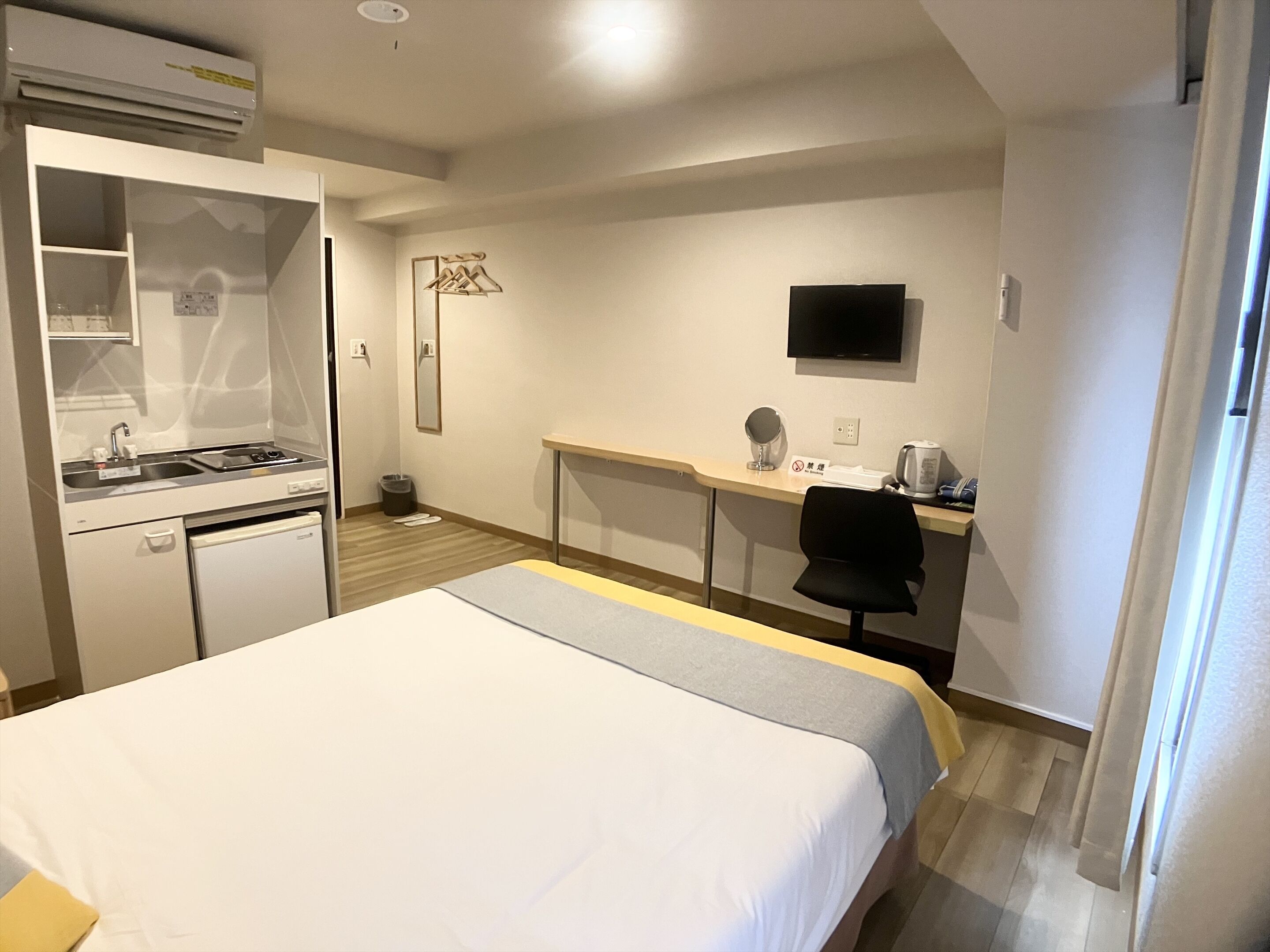 A hotel room with a bed, a desk with a chair, a television, and a kitchenette.