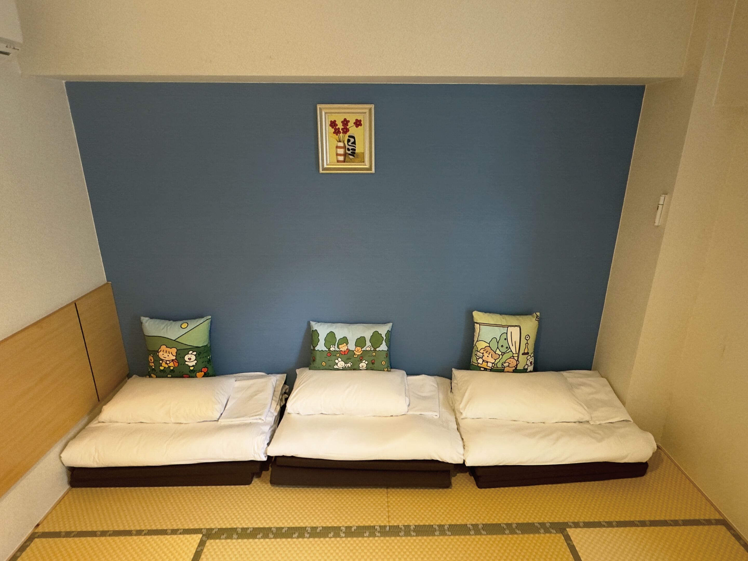 Habitación con tres camas dispuestas contra una pared azul, cada una con un diseño de almohada diferente.