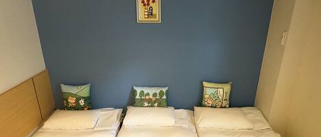 Habitación con tres camas dispuestas contra una pared azul, cada una con un diseño de almohada diferente.