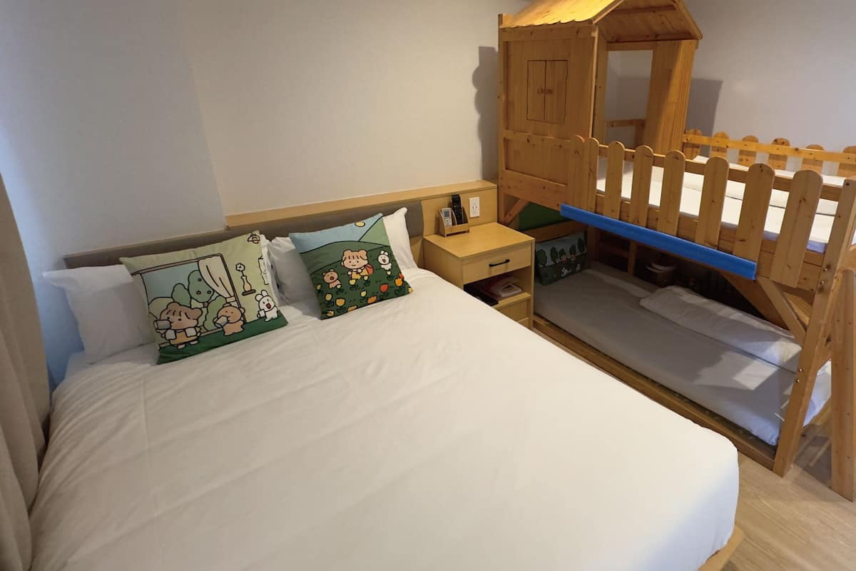 A bedroom with a bed, bedside table, and a wooden playhouse structure.