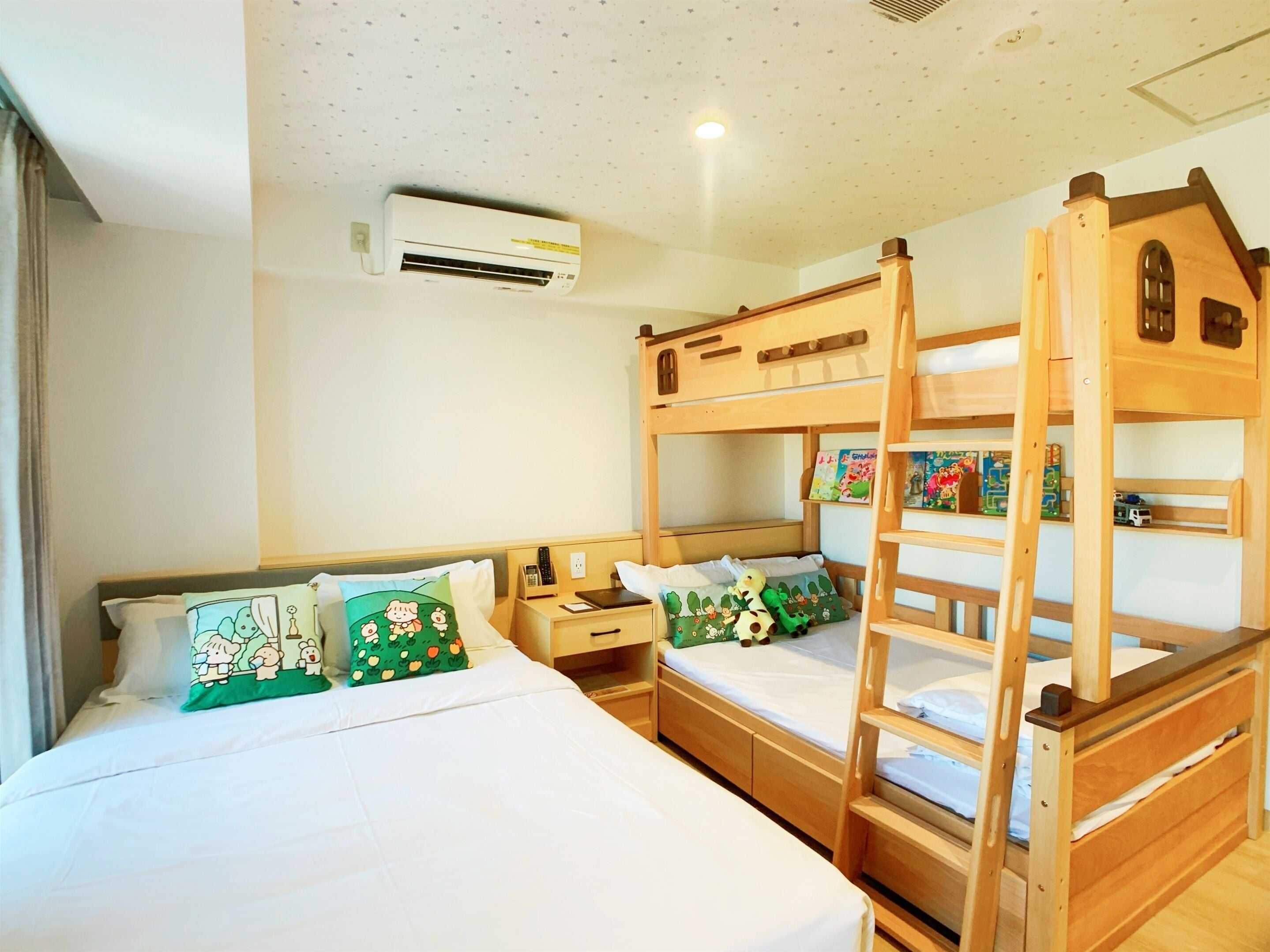 Une chambre avec un lit superposé, une échelle en bois, une table de chevet, une petite table et un appareil de climatisation fixé au mur.