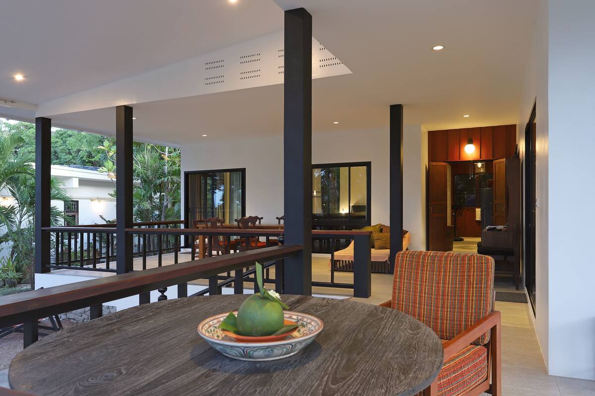 Un espacio interior amplio con una mesa de comedor de madera, un bol de fruta y un sillón con estampado.