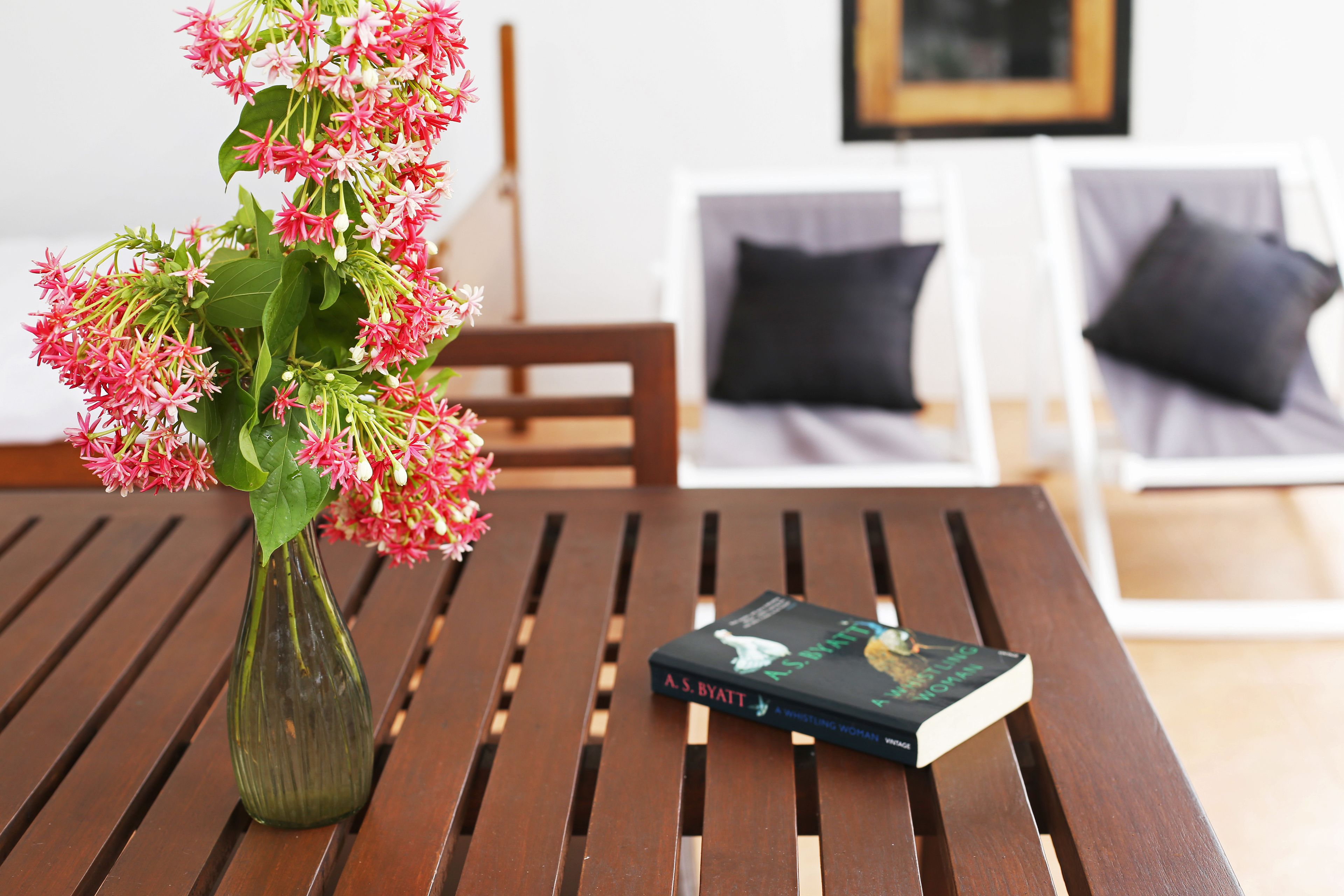 A wooden table with a book and a vase of flowers.