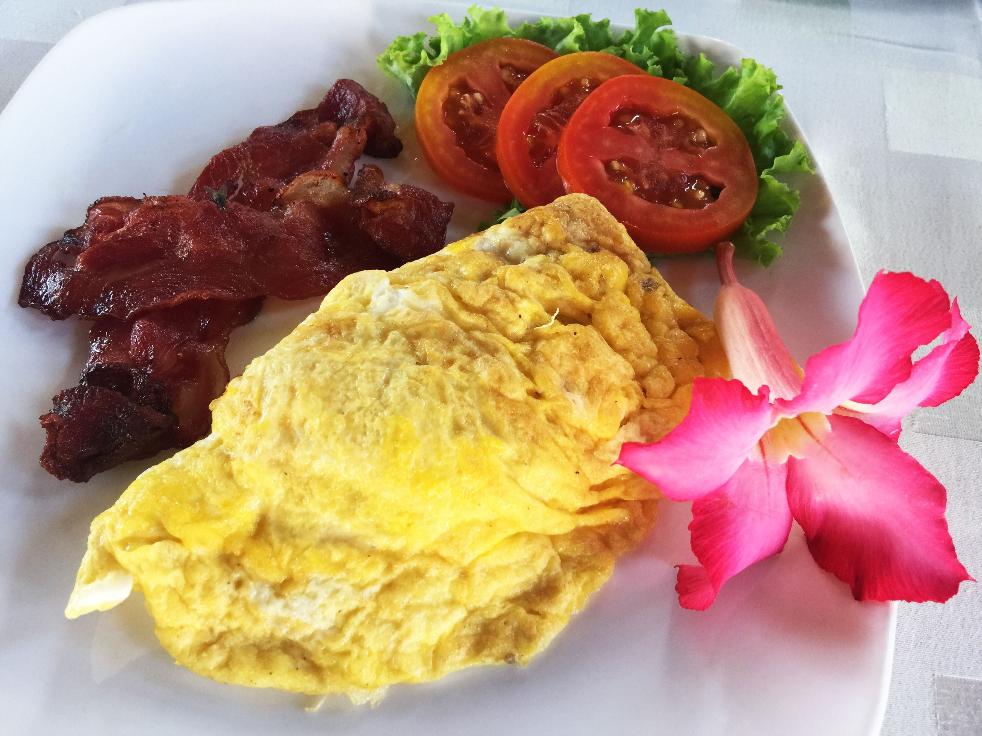 Un plato con tocino, una tortilla y tomates en rodajas sobre un plato blanco.