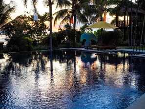 A tranquil pool area with a clear view of the water, surrounded by palm trees and a wooden deck with lounge chairs. - Villa L'Orange Bali (Gianyar)