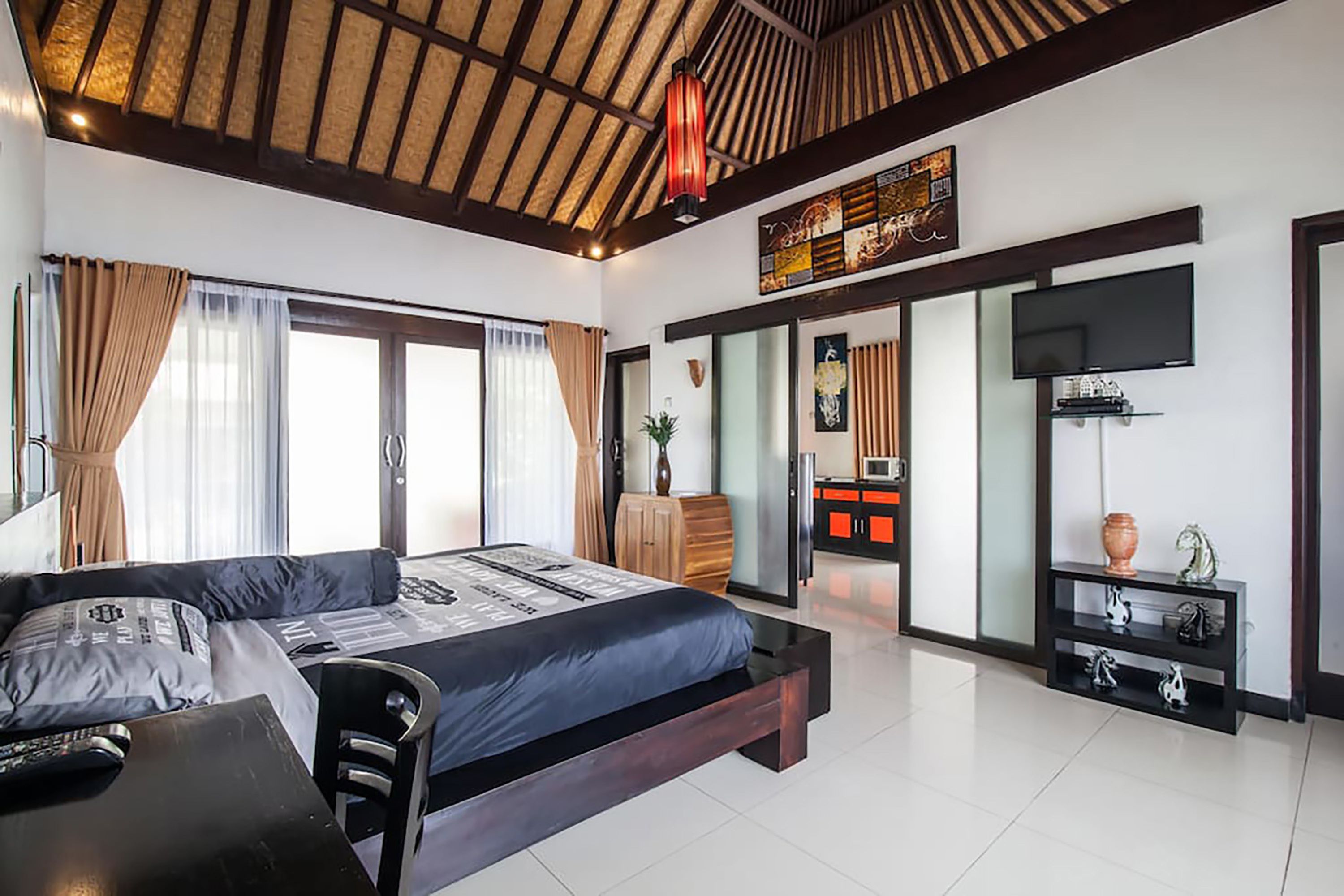 A modern hotel room with a large bed, a desk, a TV, and a kitchen area.