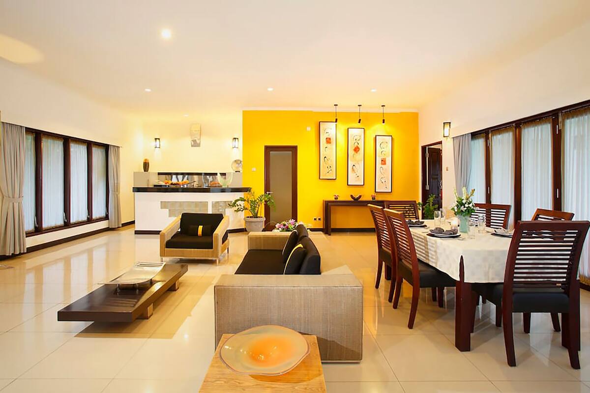 A modern living room with a dining area, featuring a sofa, a coffee table, and a dining table set for four.