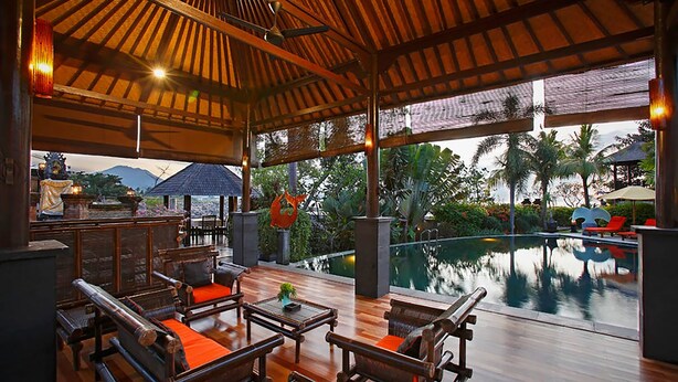 An outdoor lounge area with wooden furniture and a pool view. - Villa L'Orange Bali (Gianyar)