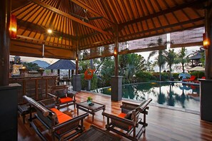 An outdoor lounge area with wooden furniture and a pool view. - Villa L'Orange Bali (Gianyar)