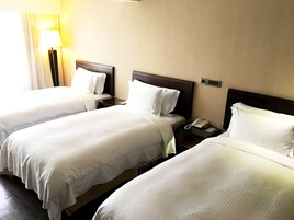 Habitación de hotel con dos camas individuales, cada una con cabecero de madera, una mesita de noche con lámpara y teléfono.