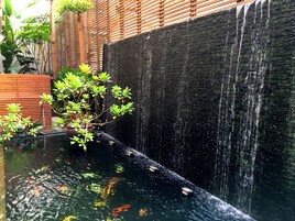 Estanque de carpas con cascada, rodeado de listones de madera y vegetación exuberante.