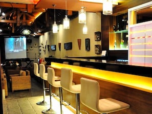 A bar area with a counter, bar stools, and a screen displaying a movie.