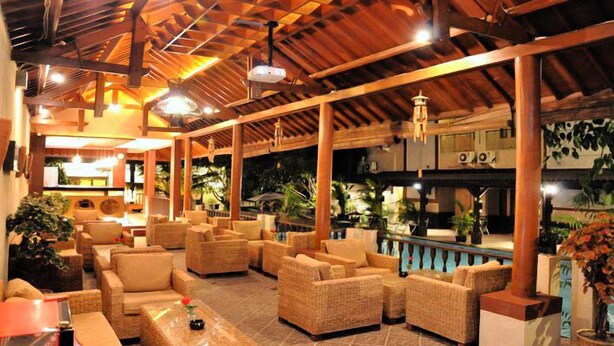 Um espaço amplo e coberto, com mobiliário de vime, piscina e vigas de madeira no teto.