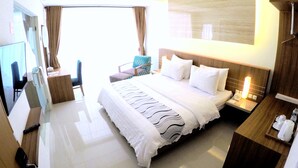 Quarto de hotel com uma cama grande, uma escrivaninha com cadeira, televisão e banheiro com chuveiro.