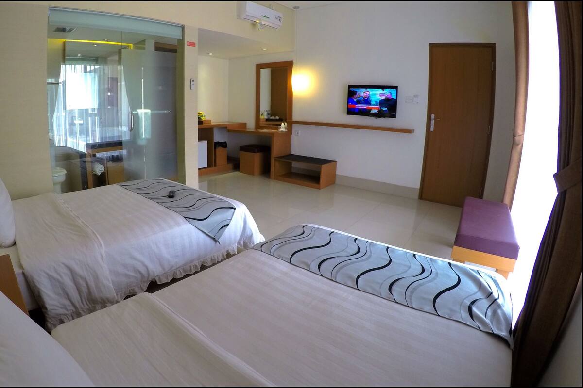 Una habitación de hotel con dos camas, un televisor en la pared, un baño y un escritorio.