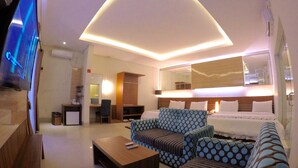 Quarto de hotel moderno com uma cama grande, um sofá, uma mesa de centro, uma escrivaninha e uma televisão.