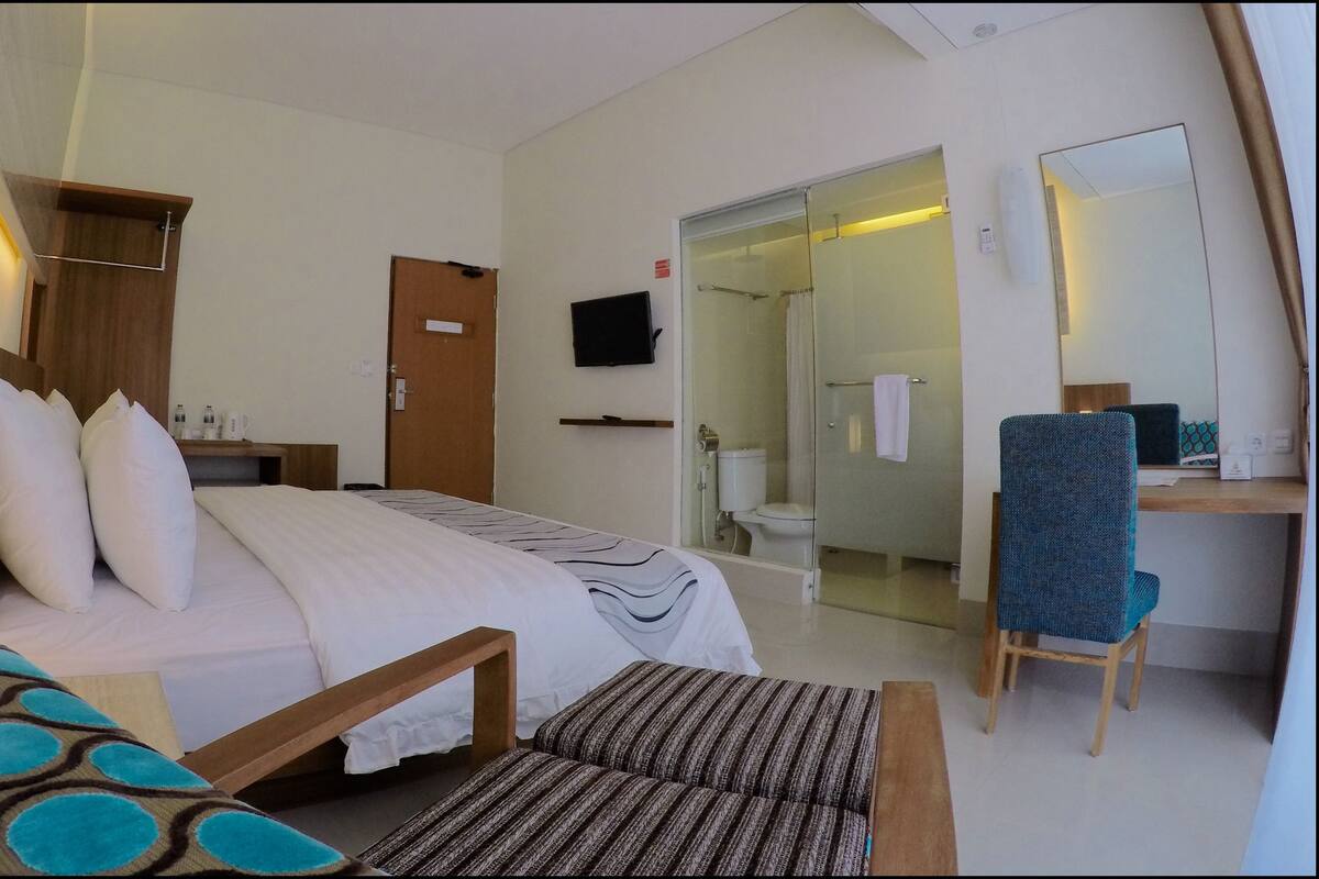 Una habitación de hotel con cama, mesita de noche, silla y baño con ducha e inodoro.