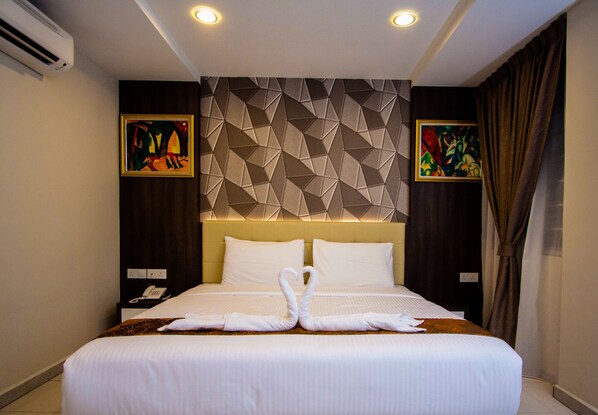 A hotel room with a large bed, two pillows, a wall-mounted phone, and two paintings on the walls. - Louis Hotel (Taiping)