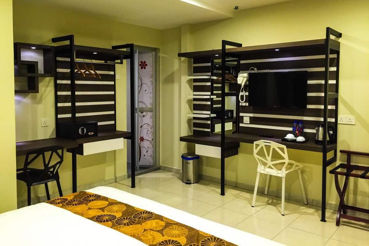 Habitación de hotel compacta con literas, un escritorio, una silla, un televisor y un cubo de basura pequeño.