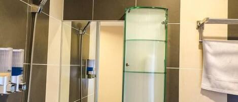 Un baño con baldosas oscuras, un armario de medicinas de vidrio, un lavabo blanco y un cabezal de ducha.
