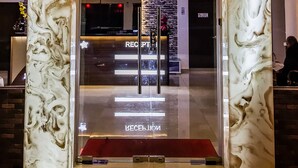 L’entrée d’un hôtel, avec une façade en marbre, un comptoir d’accueil et un lustre.