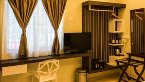 Une chambre d’hôtel équipée d’une télévision à écran plat, d’une petite étagère avec des articles de toilette, d’un sèche-cheveux et d’une poubelle.