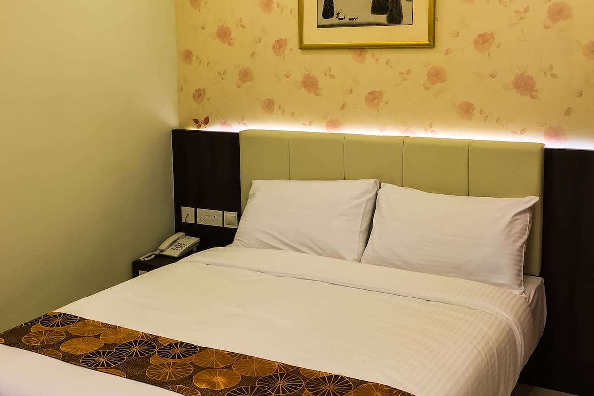 Habitación de hotel con una cama, una mesita de noche con un teléfono, una pared con papel tapiz floral y un cuadro enmarcado sobre la cama.